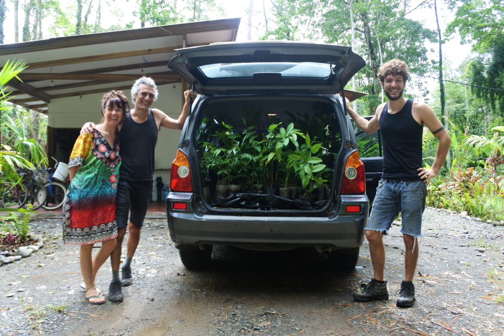 Three people next to a car with trees